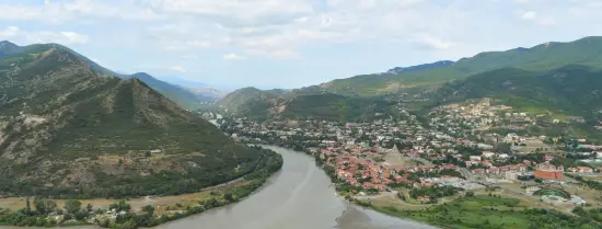 The image shows the Kura and Aragvi rivers converging into one another. In the background is also lush greenery, mountains and homes.